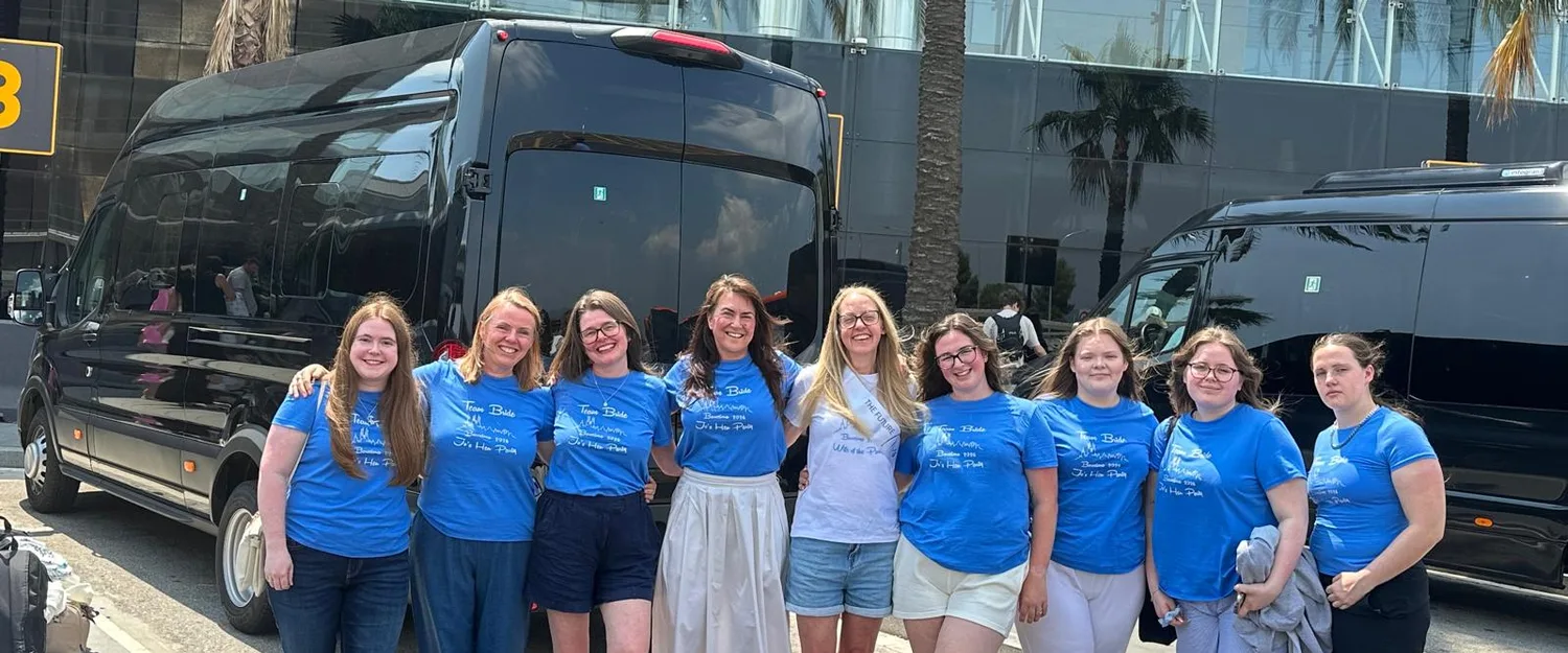Group of passengers in matching blue t-shirts in front of two black BCN Minibus vans