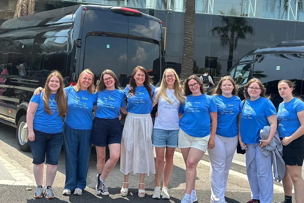 Group of passengers in matching blue t-shirts in front of two black BCN Minibus vans