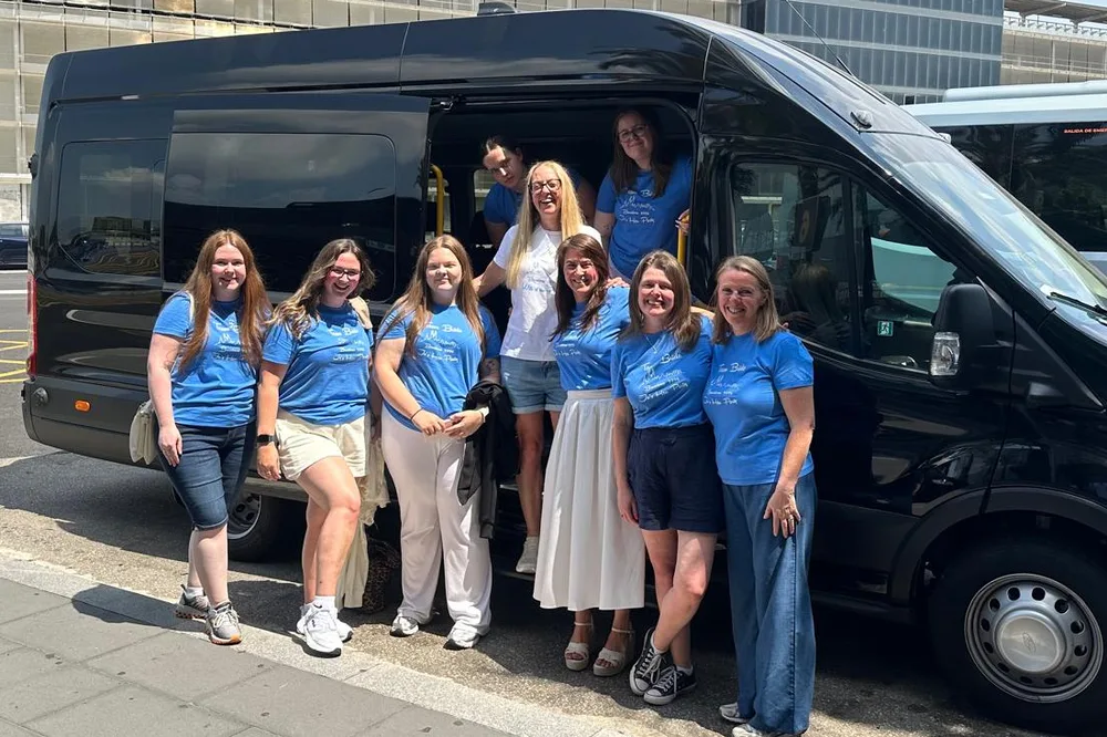 Group of passengers in matching blue t-shirts with a black BCN Minibus van